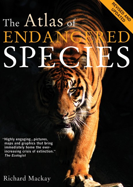 Book cover for The Atlas of Endangered Species. A close-up photo extends to all edges showing a tiger emerging from a black background with its left foreleg resting on a stone block. Half its face and remaining limbs are veiled in darkness. Text is white cream or amber.