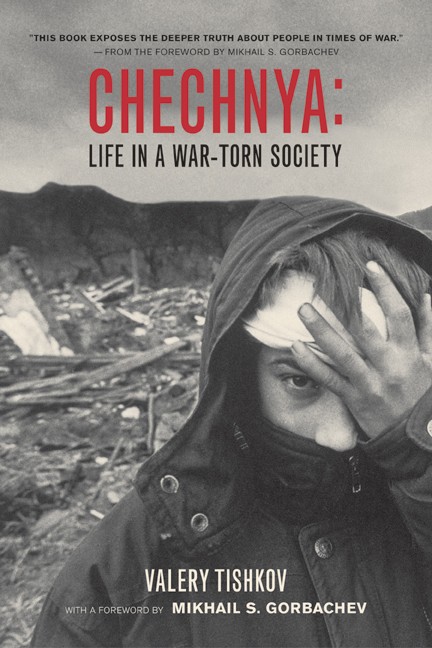 Book cover for Chechnya. A black-and-white photo extends to edges showing a hooded person with a bandaged forehead hand pressed to his temple. The background is blurred and rubble-strewn. Text is black and white with a bold red title.